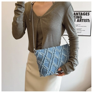 Close-up of light blue denim crossbody bag with frayed diamond pattern and metal chain