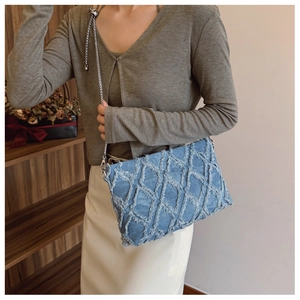 Detail of blue denim shoulder bag featuring frayed diamond quilt and silver chain strap