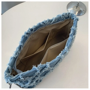 Detail view of denim underarm bag showing fringed edges and interior pocket layout