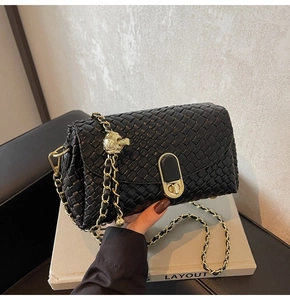 Detail of black woven shoulder bag with gold chain strap and spherical metal ornament