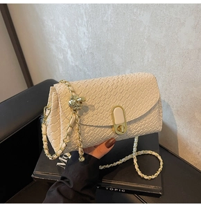 Close-up of beige crocodile texture handbag with gold chain and spherical metal detail