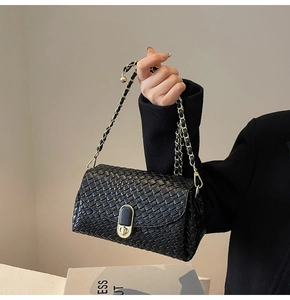 Detail of black woven leather handbag with gold chain strap and elegant metal clasp