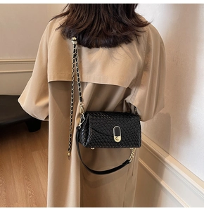 Detail of a black woven pillow bag featuring a gold buckle and luxury chain strap