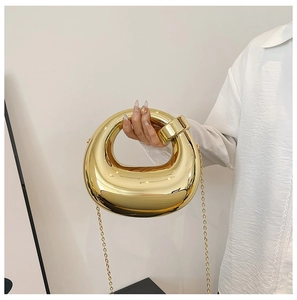 Close-up of golden acrylic box evening bag with round handle and metallic chain strap