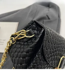 Close-up of black woven leather pillow bag featuring chunky gold chain and metal hardware