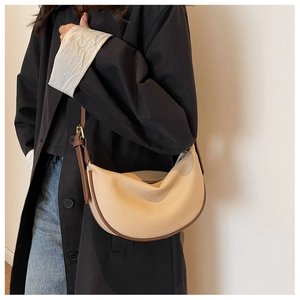 Borsa a mezzaluna beige con bordo marrone indossata a spalla in una scena di vita