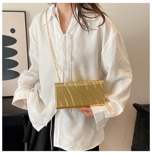 Détail d'une pochette dorée métallique avec texture ondulée et fine bandoulière chaîne