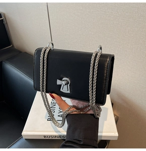 Detail view of the elegant silver keyhole-shaped lock and woven metal chain on the black bag