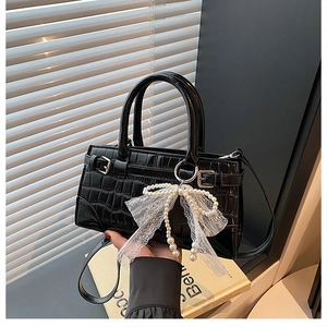 Close-up of black stone texture handbag with a pearl bow pendant and crossbody strap