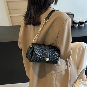 Chic black woven texture shoulder bag with gold chain strap on a model in a cafe