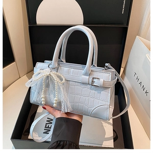 Detail of light blue croc-embossed handbag with pearl lace bow charm in luxury gift box