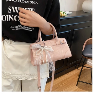 Detail of pink faux leather bag with crocodile texture and pearl lace bow pendant