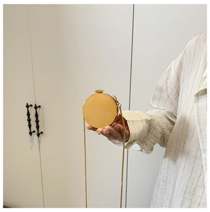 Detailed view of a golden circular mini clutch bag with a slim metal chain strap
