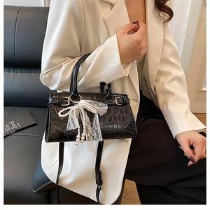 Close-up of black crocodile pattern handbag with elegant white lace pearl bow pendant detail
