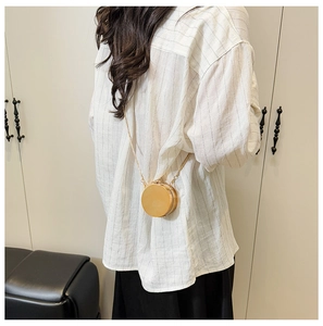 Detailed close-up of a mini round gold metallic crossbody bag with fine chain strap