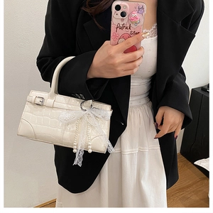 Close-up of white crocodile pattern handbag with pearl bow charm and silver buckle