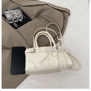 Detail of white crocodile pattern handbag with pearl bow and lace decoration