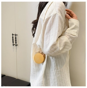 Detailed view of a mini round gold metallic hardshell bag with a thin chain shoulder strap