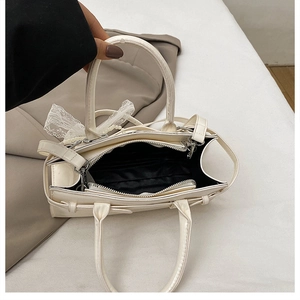 Detail view of cream white stone-patterned bag with internal zipper and lace bow