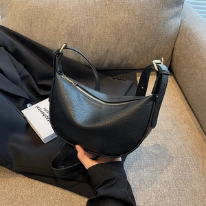 Elegante borsa a mezzaluna in pelle nera con cerniera dorata su divano grigio