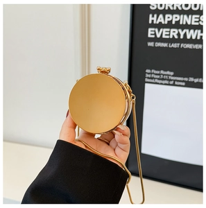 Detail of a round gold mini chain bag with a mirror finish and metallic clasp handle