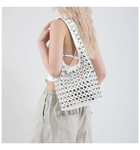 Close-up of a white leather shoulder bag featuring silver rivets on a female model
