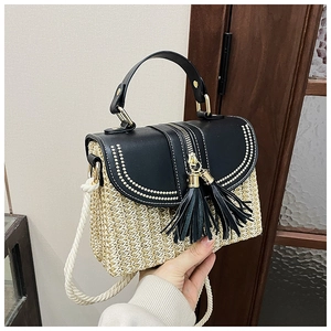 Detail of straw woven crossbody bag featuring black leather trim and twin tassels