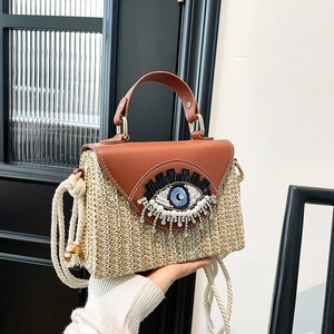 Handwoven straw shoulder bag with brown leather flap and beaded eye embroidery detail