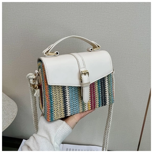 Detail of colorful woven straw bag with white leather flap and gold buckle closure