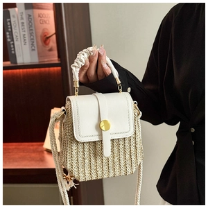 Detail of woven straw handbag with white leather flap and circular gold metal clasp