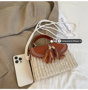Detail view of woven straw bag with leather flap and tassels beside a smartphone for size reference