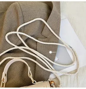 Detail of woven rope shoulder strap and gold hardware on beige straw crossbody bag