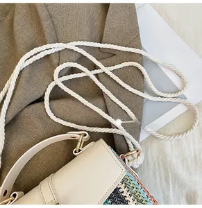 Detail of woven straw shoulder bag featuring thick cotton rope strap and metal hooks