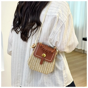 Detail of woven straw and brown leather shoulder bag with gold hardware on a model