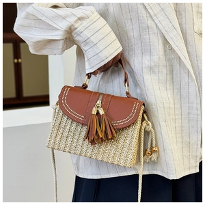Detail of straw crossbody bag with brown faux leather flap and tassel accents