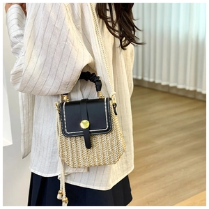 Detail of woven straw bag with black leather flap and gold clasp on a model