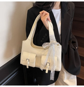 Close-up of cream shoulder bag with dual front pockets and lace bow detail
