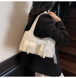 Detail of cream white shoulder bag with twin pockets and decorative lace ribbon bow
