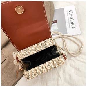 Detail view of woven straw bag with brown leather flap and white rope shoulder strap