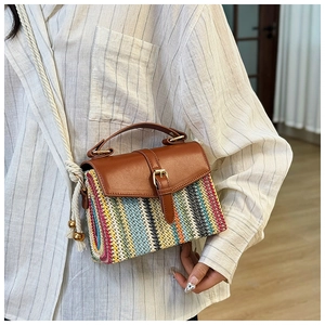 Detail of colorful woven straw bag featuring brown leather flap and rope shoulder strap