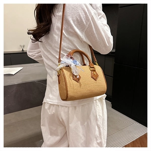 Détail du sac cylindrique en paille tressée avec poignées en cuir et nœud en dentelle