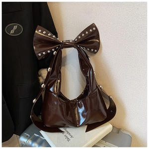 Detail of dark brown patent leather shoulder bag with large bow and silver studs