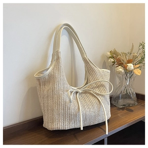 Detailed texture of hand-woven beige straw tote bag featuring a leather bow accent