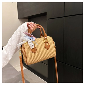 Détail du sac cylindrique tressé avec poignées en cuir et nœud en ruban à carreaux