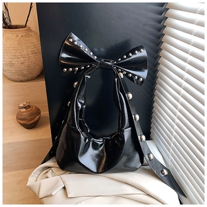 Detail of black patent leather bag featuring a large bow and silver metal stud accents