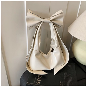 Close-up of cream faux leather underarm bag with oversized bow and silver studs