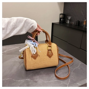Détail du sac boston en paille tressée avec bordure en cuir brun et nœud décoratif