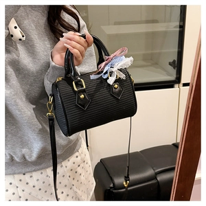 Détail d'un sac tonneau noir texturé avec un nœud en dentelle à carreaux rouge et bleu