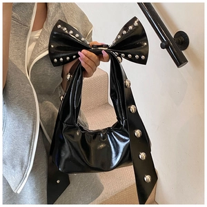 Detail of black patent leather bag featuring a large bow and silver studs on the handle