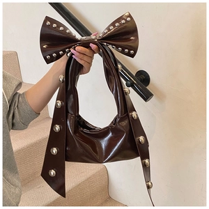 Close-up of dark brown patent leather handbag featuring oversized bow with silver rivets